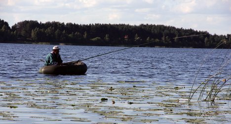 Рыбак в резиновой лодке ловит рыбу на озере заросшем кувшинками
