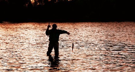 Силуэт рыбака на фоне заката выловил рыбу на спиннинг