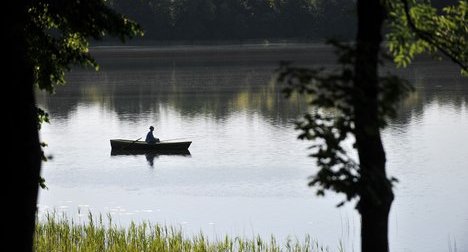 Рыбак в лодке ловит рыбу на удочку на лесном озере